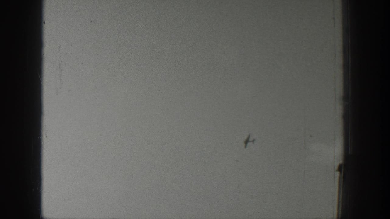 Wyoming 1939 home-movie frame with a tiny aircraft or bird-like speck over a pale sky, flat waterline, and distant shore.