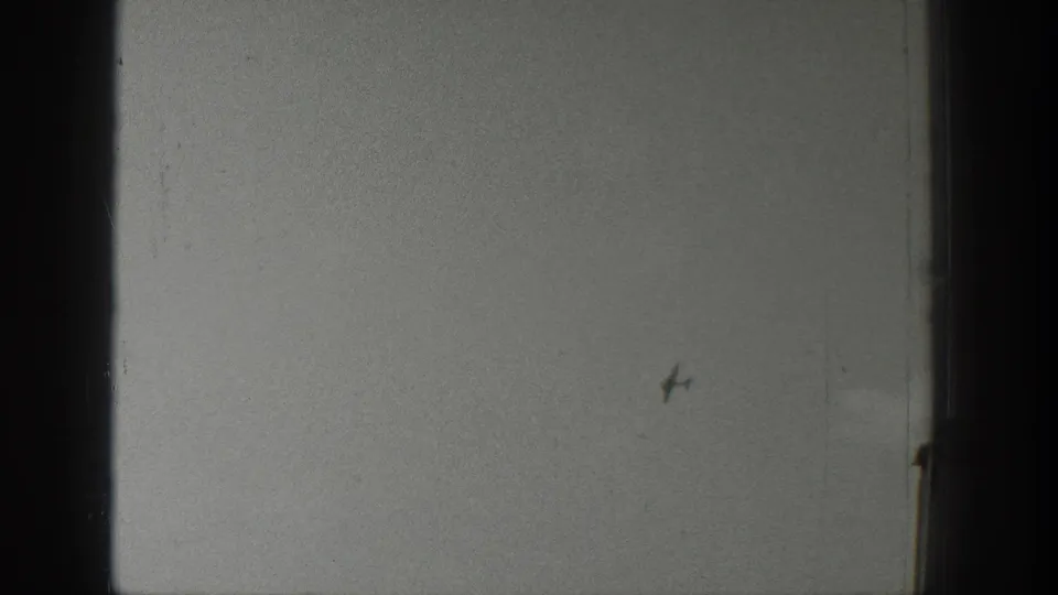 Wyoming 1939 home-movie frame with a tiny aircraft or bird-like speck over a pale sky, flat waterline, and distant shore.