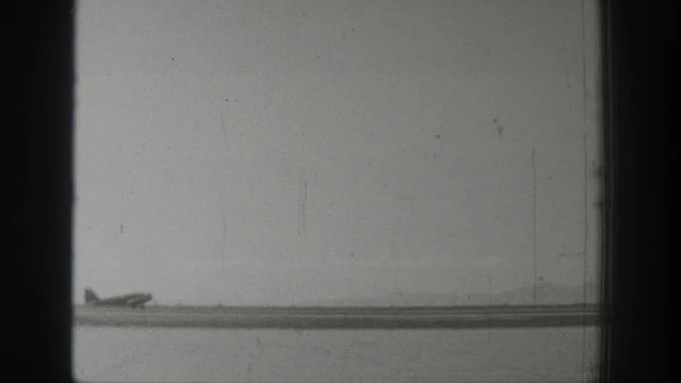 Wyoming 1939 frame showing a small propeller airplane on or near a riverside runway under a pale overcast sky.