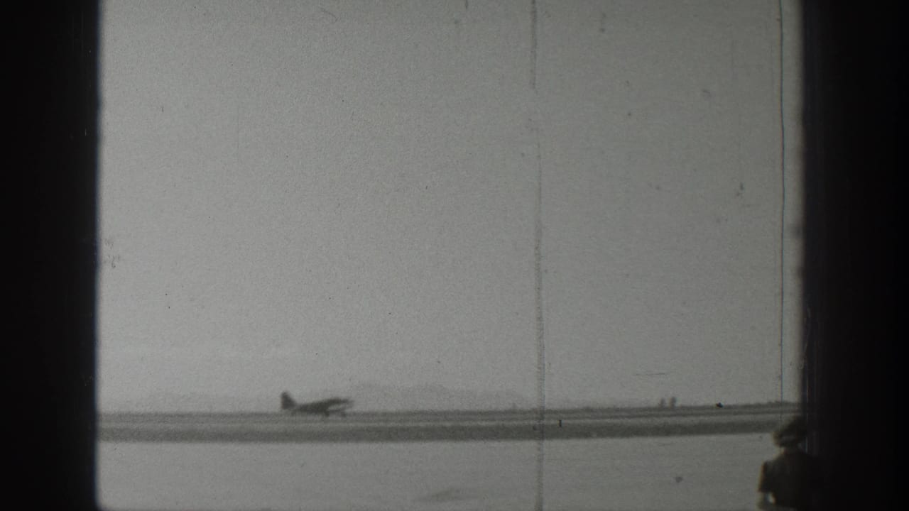 1939 Wyoming 8mm frame showing a small propeller airplane on a runway, with dark vertical frame edges and a hazy airfield background.