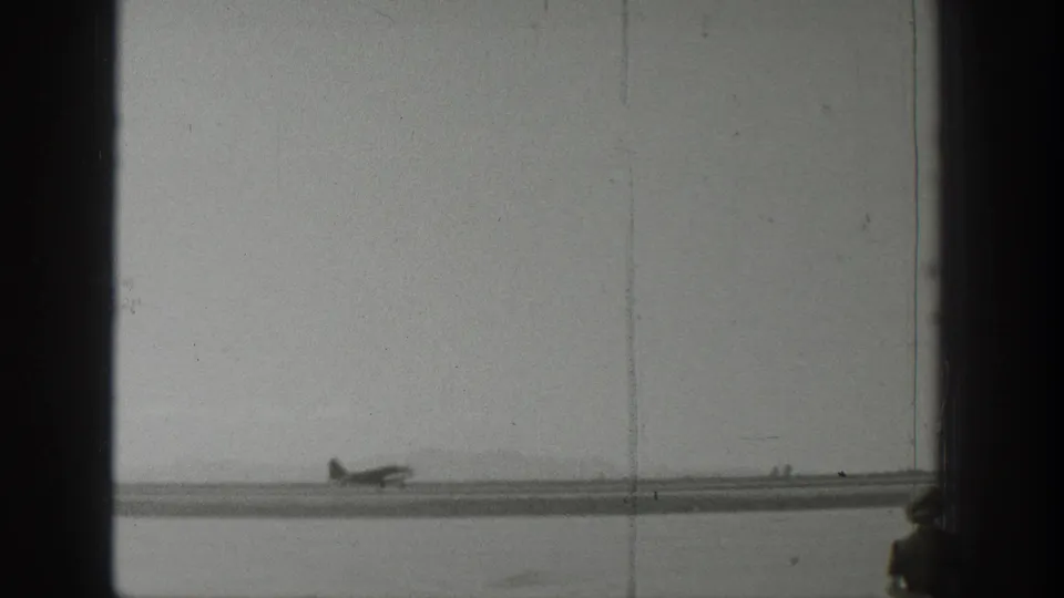 1939 Wyoming 8mm frame showing a small propeller airplane on a runway, with dark vertical frame edges and a hazy airfield background.