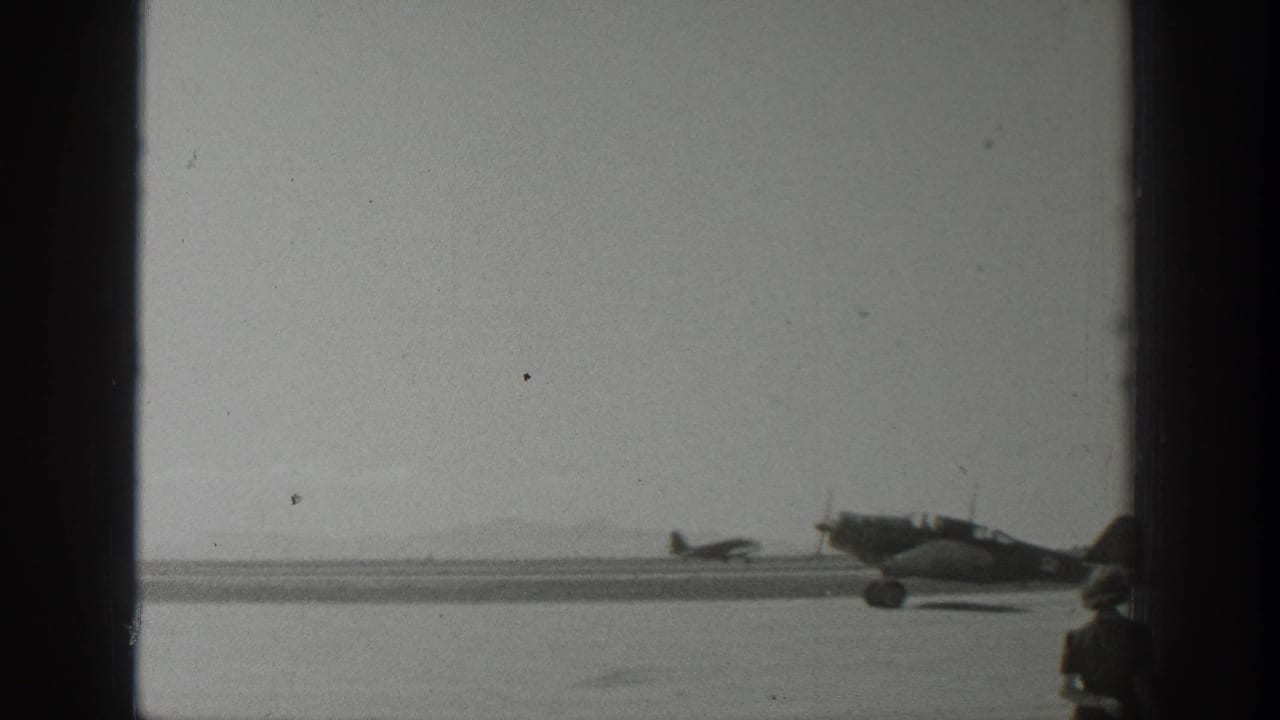 1939 Wyoming 8mm frame with a propeller airplane on the runway and a partially visible foreground spectator near the edge of the shot.