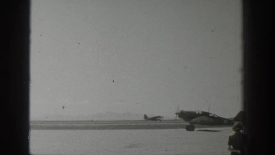 1939 Wyoming 8mm frame with a propeller airplane on the runway and a partially visible foreground spectator near the edge of the shot.