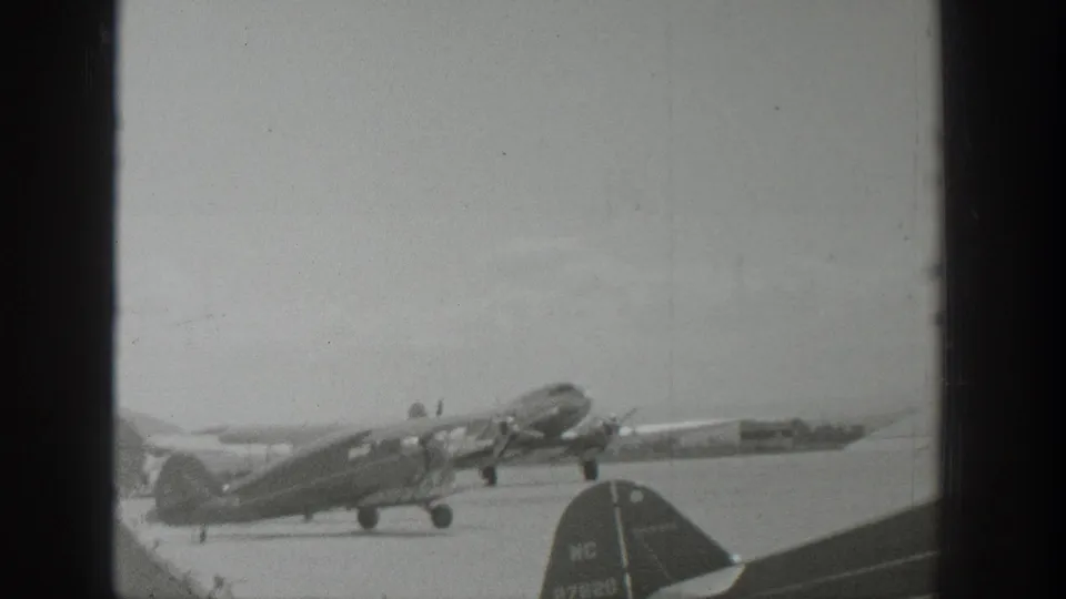 1939 Wyoming 8mm frame showing a propeller airplane angled upward on the runway, with another aircraft tail visible in the foreground.