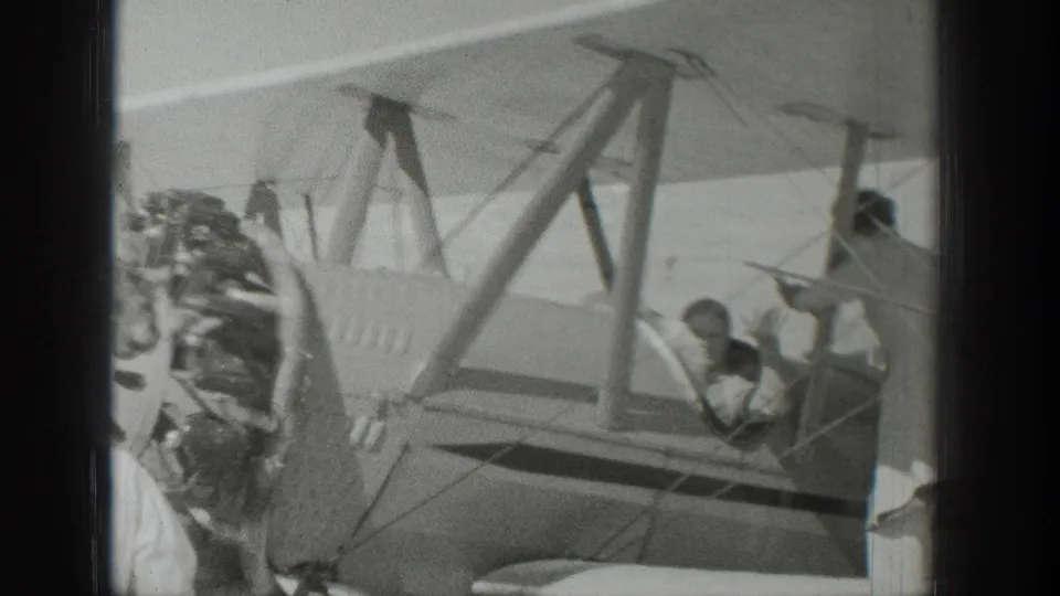 1939 Wyoming frame with a pilot in an open cockpit and onlookers gathered near the biplane wing and fuselage.