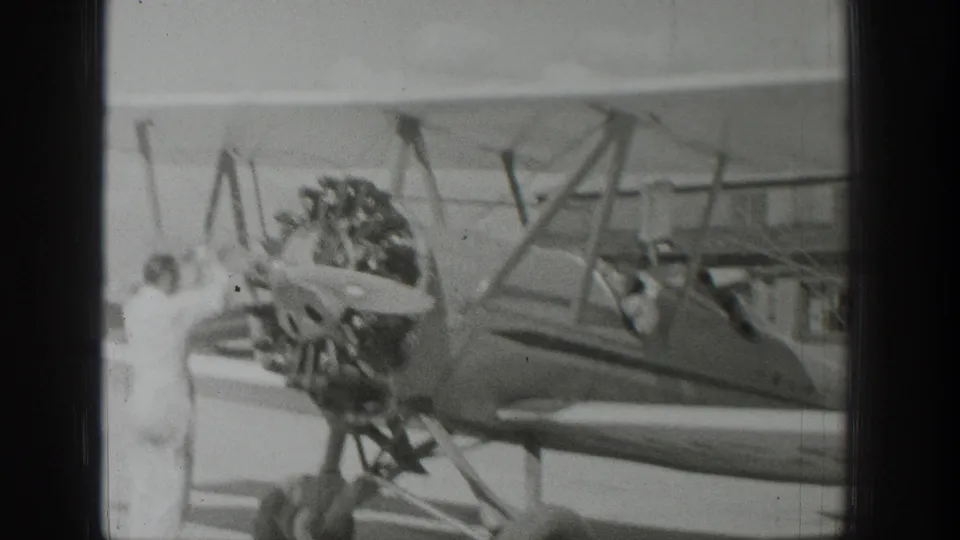 1939 Wyoming airfield frame showing a person at the biplane nose near the radial engine, propeller, landing gear, and open cockpit.