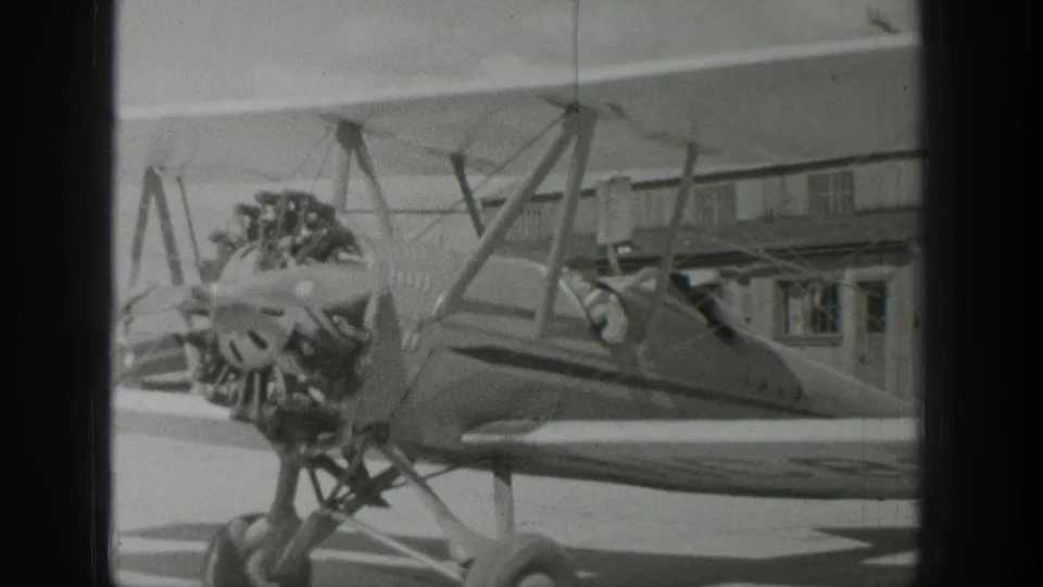 1939 Wyoming footage shows the biplane from the side, emphasizing the radial engine, open cockpit, wing struts, and hangar setting.