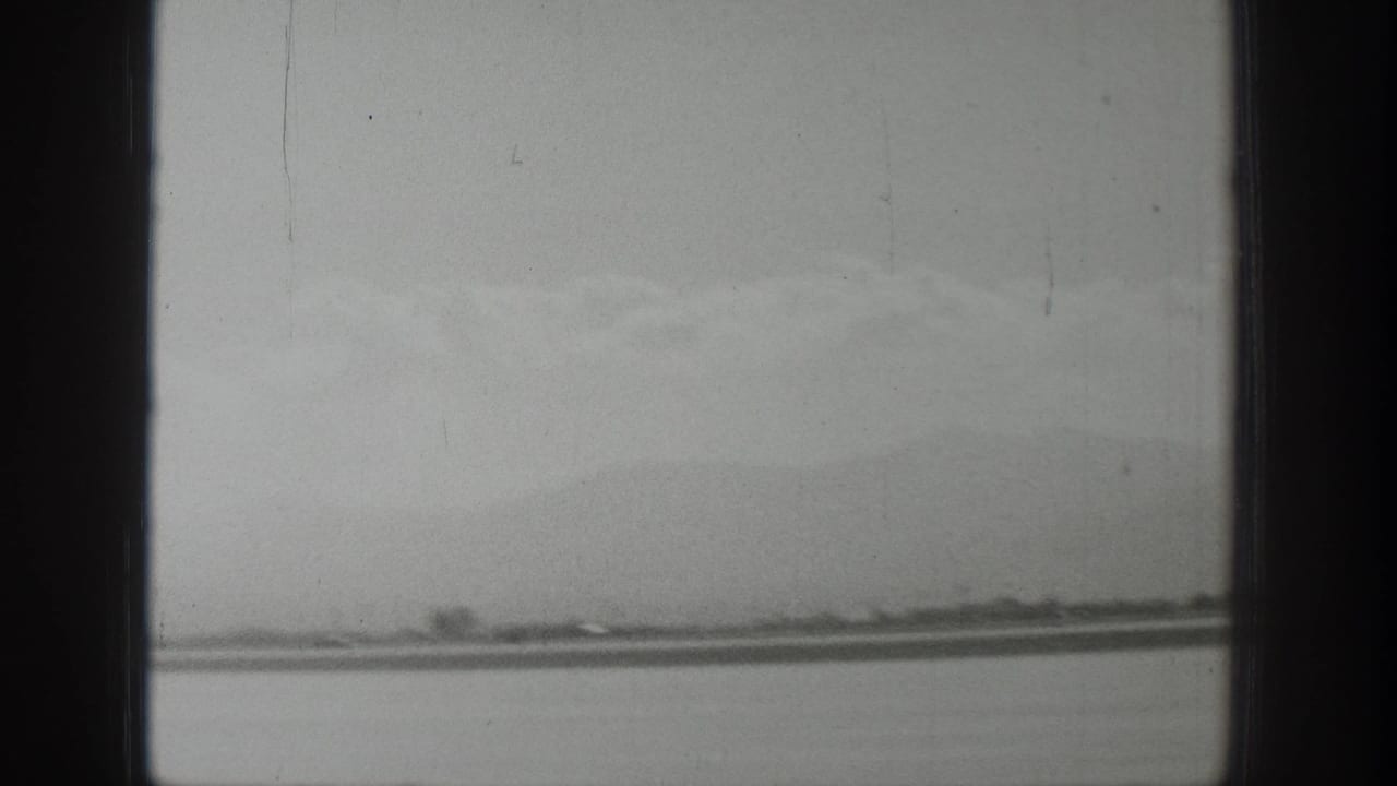 Wyoming 1939 home-movie frame showing a distant airstrip, low horizon, hazy mountains, and dark window-frame bars in the foreground.