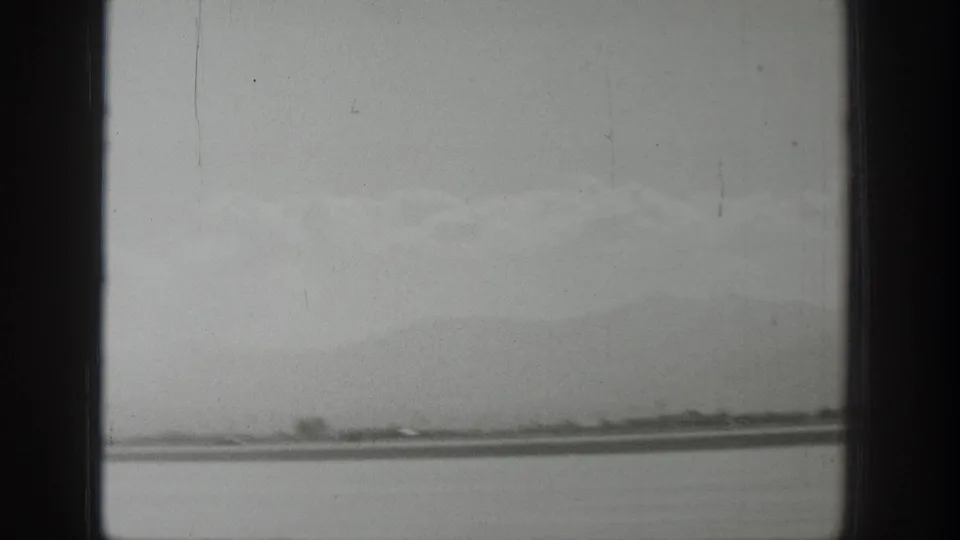 Wyoming 1939 home-movie frame showing a distant airstrip, low horizon, hazy mountains, and dark window-frame bars in the foreground.
