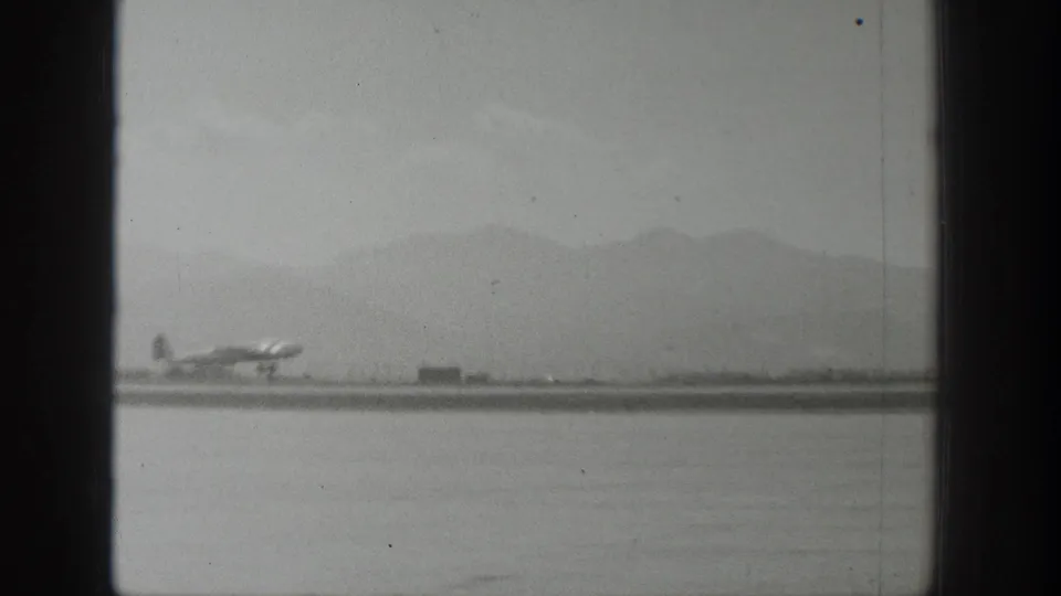 Wyoming 1939 frame with a small propeller airplane low on the runway, seen at distance beneath hazy mountains through window framing.