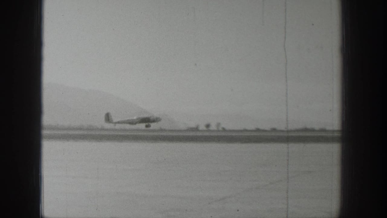 A distant propeller airplane sits or moves along a Wyoming runway in black-and-white 1939 home-movie footage.