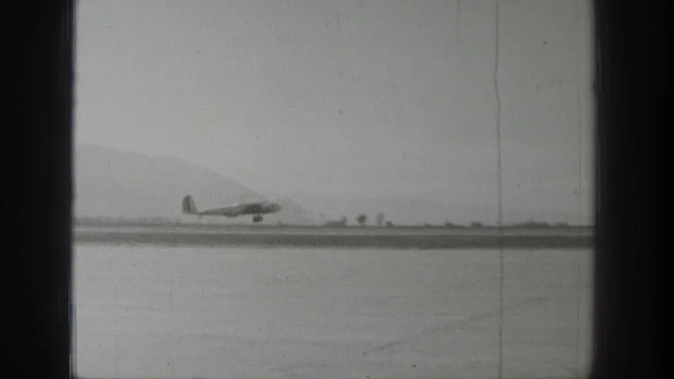 A distant propeller airplane sits or moves along a Wyoming runway in black-and-white 1939 home-movie footage.