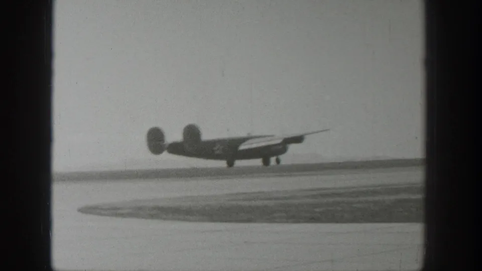 A propeller airplane rises just above the runway during takeoff in Wyoming, captured in soft black-and-white 8mm footage.
