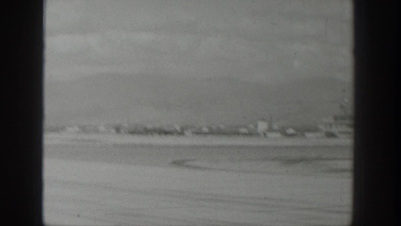 1939 Wyoming 8mm aerial view through an airplane window, showing flat open land, a distant settlement line, and mountains beyond.