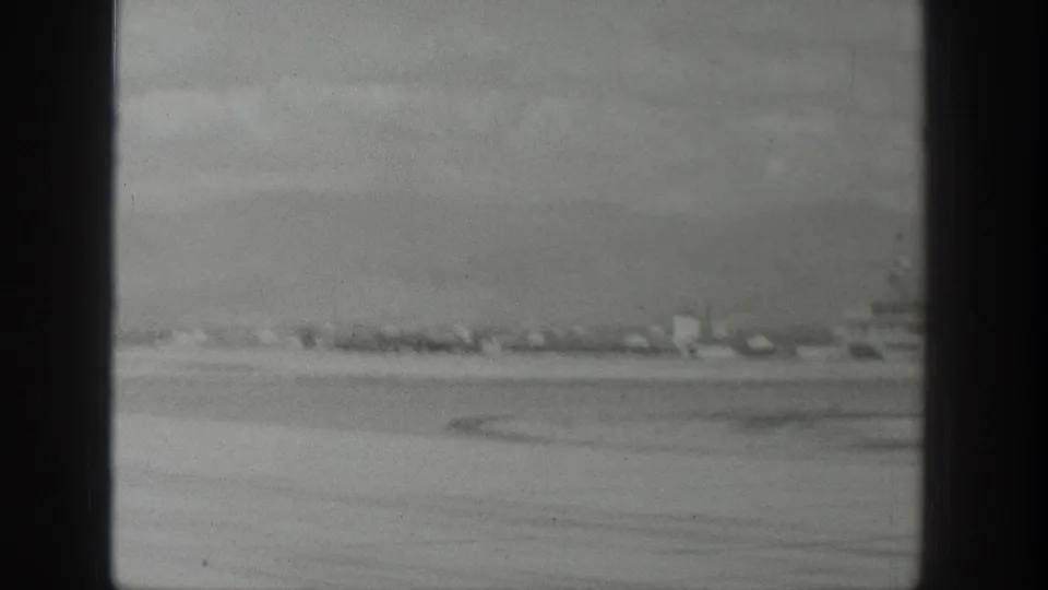 1939 Wyoming 8mm aerial view through an airplane window, showing flat open land, a distant settlement line, and mountains beyond.
