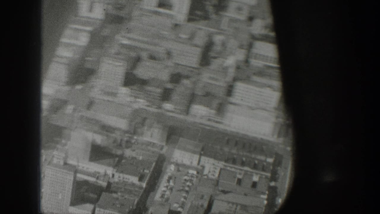 1939 Wyoming home-movie frame showing a soft aerial view of dense city blocks and streets through dark aircraft framing.