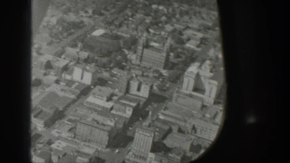 Aerial 8mm frame from the Wyoming clip showing urban buildings and streets from a passenger viewpoint.