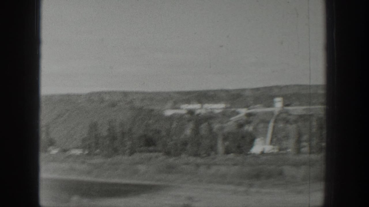1939 Wyoming travel footage shows a distant hillside, sparse trees, and utility structures viewed through a dark vehicle or window frame.