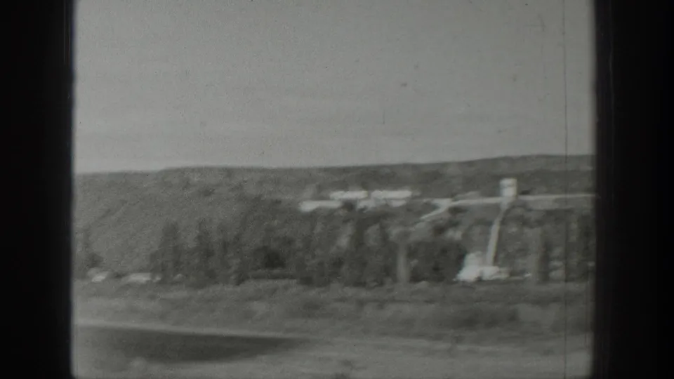 1939 Wyoming travel footage shows a distant hillside, sparse trees, and utility structures viewed through a dark vehicle or window frame.