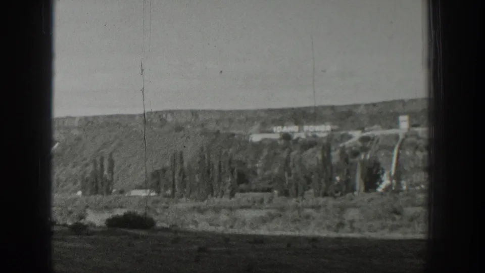 The IDAHO POWER lettering appears on a distant hillside in 1939 Wyoming footage, with trees, dry ground, and utility structures nearby.