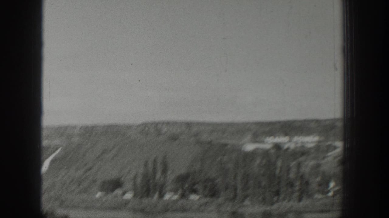 1939 Wyoming 8mm frame showing rolling hills, scattered trees, distant structures, and a clear pale sky through dark gate edges.