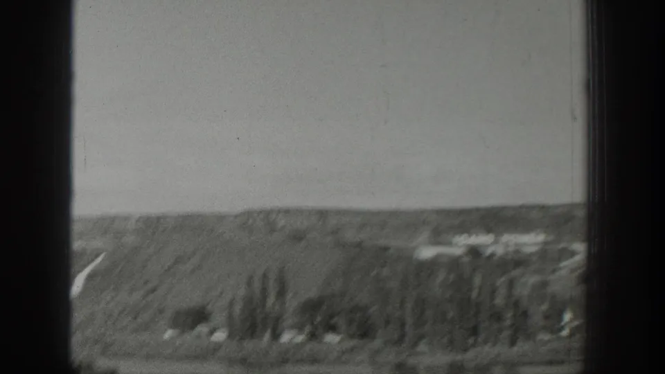 1939 Wyoming 8mm frame showing rolling hills, scattered trees, distant structures, and a clear pale sky through dark gate edges.