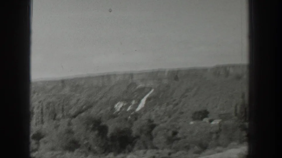 1939 Wyoming 8mm frame showing rolling terrain, scattered trees, a field foreground, and pale hillside markings beneath a clear sky.