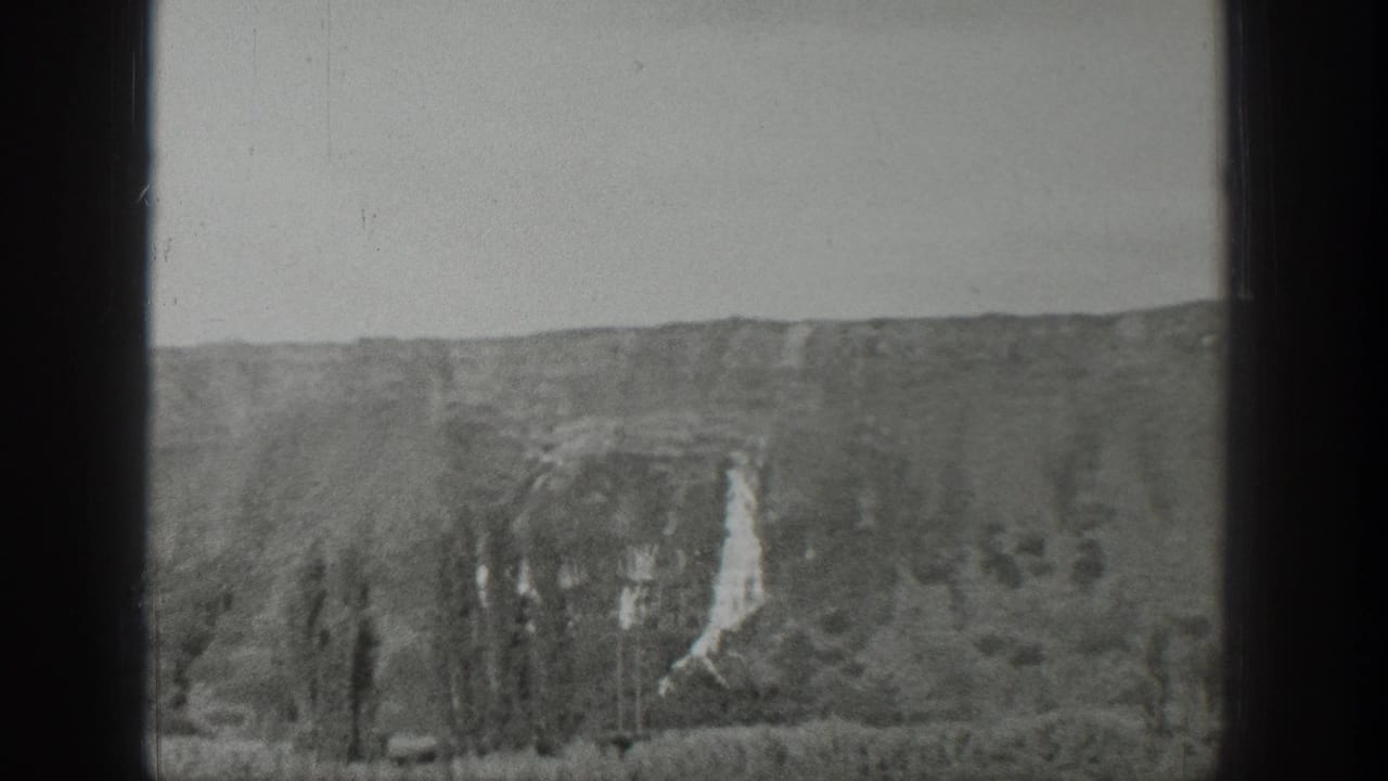 1939 Wyoming landscape view showing a rocky cliff face, pale waterfall-like streak, low trees, and open sky.