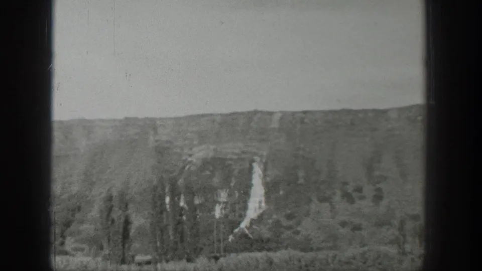 1939 Wyoming landscape view showing a rocky cliff face, pale waterfall-like streak, low trees, and open sky.