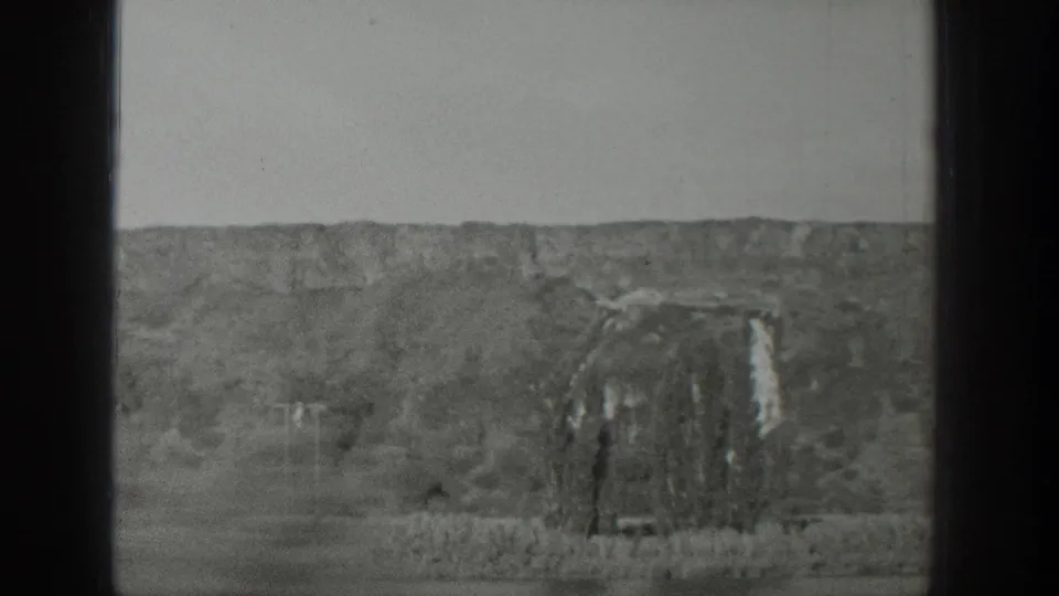 1939 Wyoming home-movie frame of a rocky hillside, pale waterfall-like feature, scrubby foreground, and soft film grain.