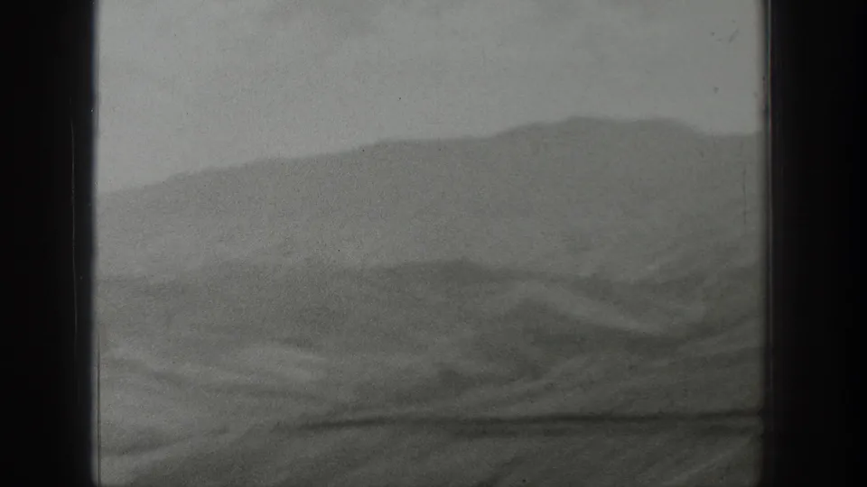 1939 Wyoming home-movie view of hazy mountain ridges seen through a dark window frame from a moving vehicle.