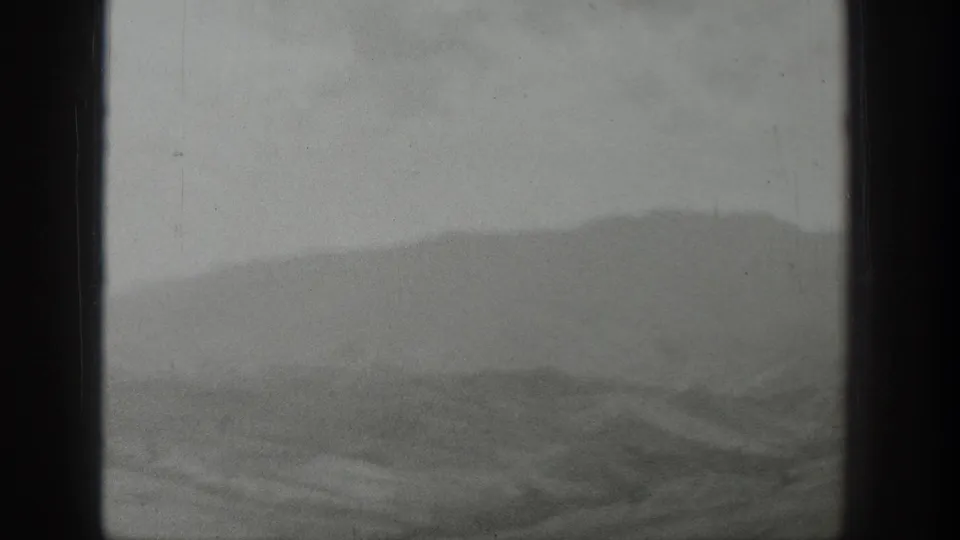 Distant Wyoming mountains and low foothills appear beyond a vertical vehicle window divider in soft 8mm footage.