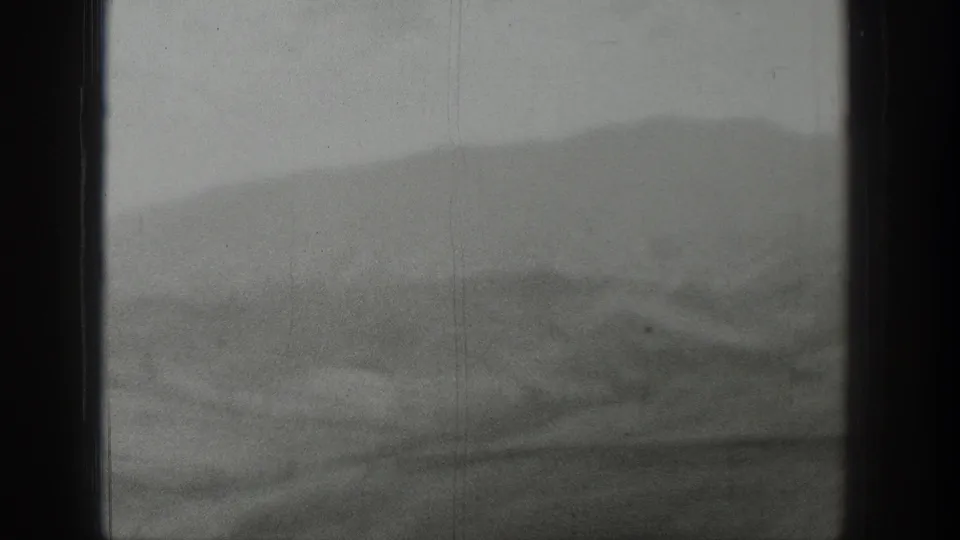 A moving-vehicle view shows blurred Wyoming foothills and a distant ridge line through a dark window edge.