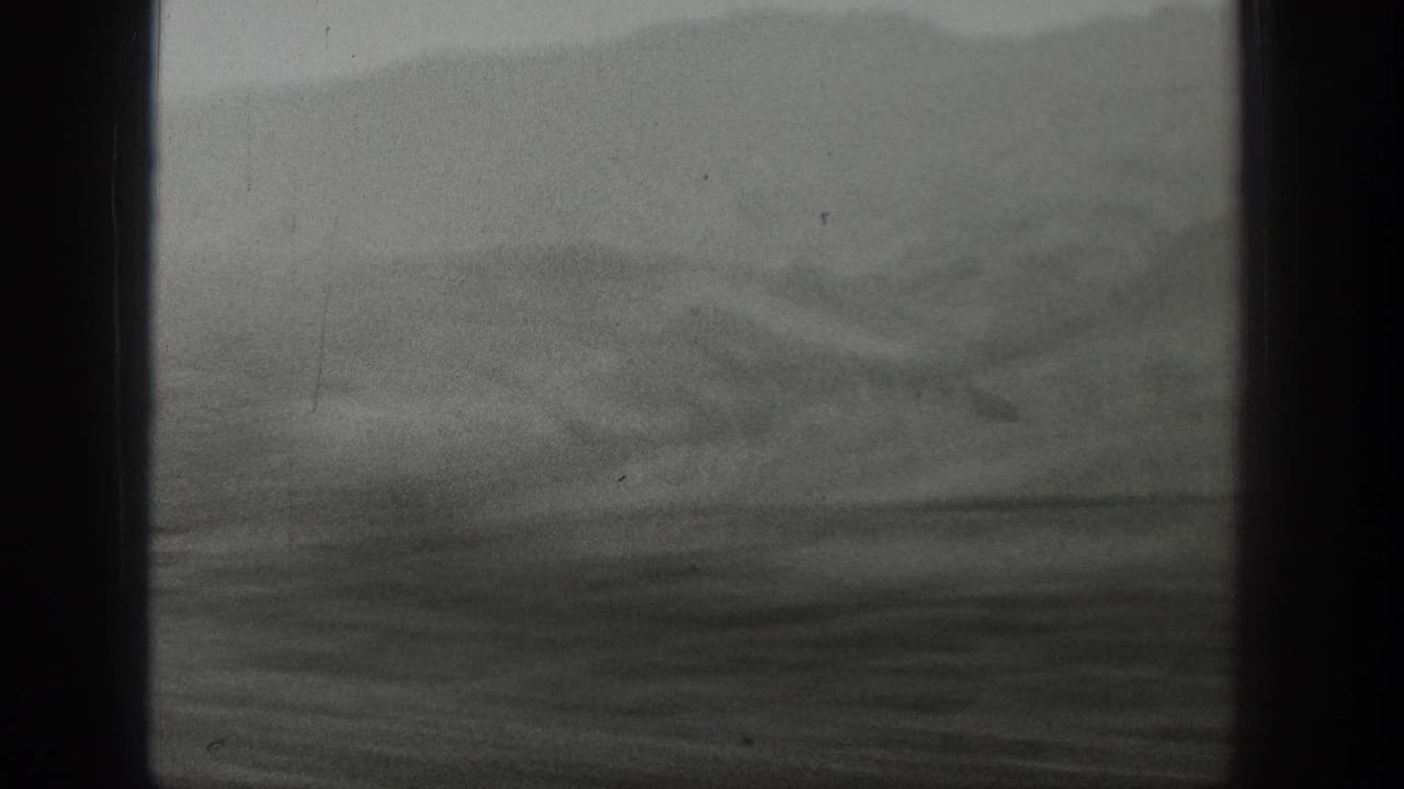 1939 Wyoming mountain terrain appears through a train window, with dark vertical framing, soft focus, and overcast haze.