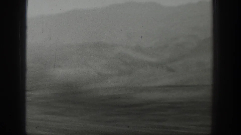 1939 Wyoming mountain terrain appears through a train window, with dark vertical framing, soft focus, and overcast haze.