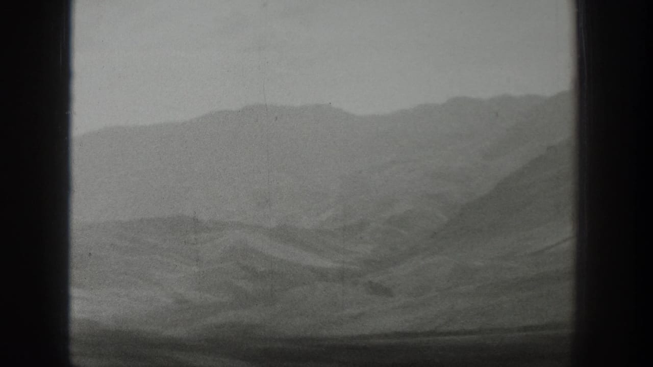 Hazy Wyoming ridges are visible through the train window, with a dark center divider and muted black-and-white 8mm texture.