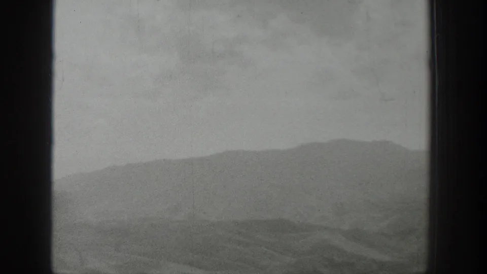 A soft black-and-white view shows low Wyoming mountains and open ground through the train window during a rail journey.