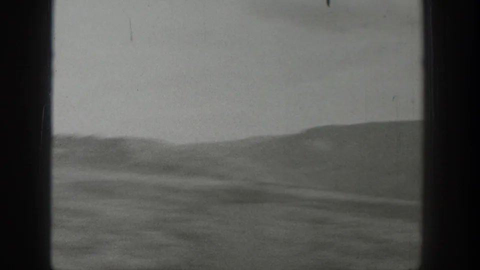 1939 Wyoming 8mm frame with low arid hills, muted ground texture, hazy sky, and visible gate edges.