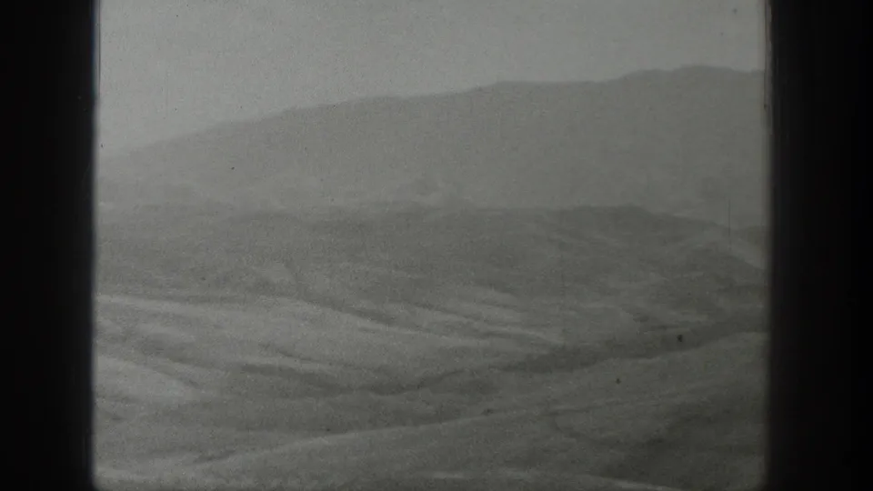 1939 Wyoming 8mm frame showing rolling arid terrain, a distant hill ridge, haze, grain, and dark gate edges.
