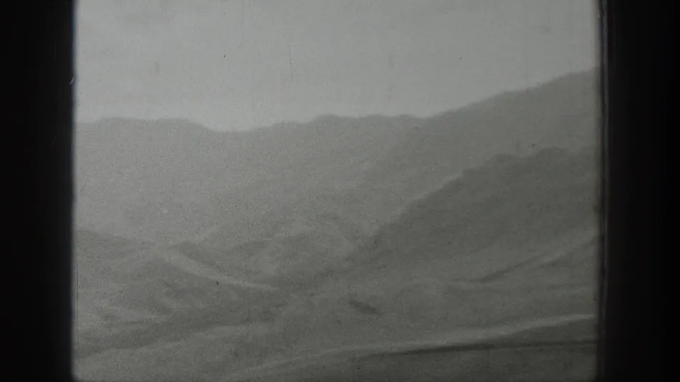 A soft black-and-white view of Wyoming hills and valley terrain through a vehicle window in 1939 8mm footage.