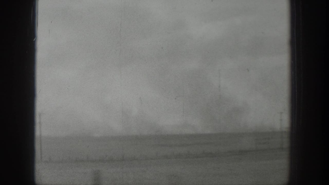 A fixed 8mm view through a window in Wyoming, showing flat rural land and a stormy gray sky.