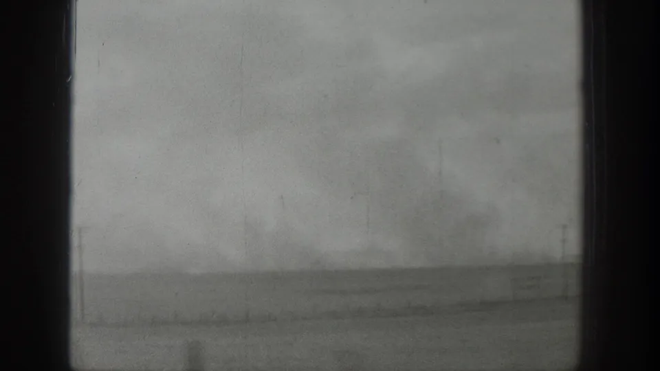 A fixed 8mm view through a window in Wyoming, showing flat rural land and a stormy gray sky.