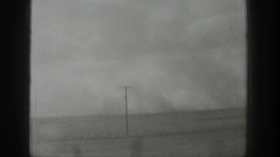 1939 Wyoming home-movie frame with a utility pole, open field, and windblown haze seen from indoors.