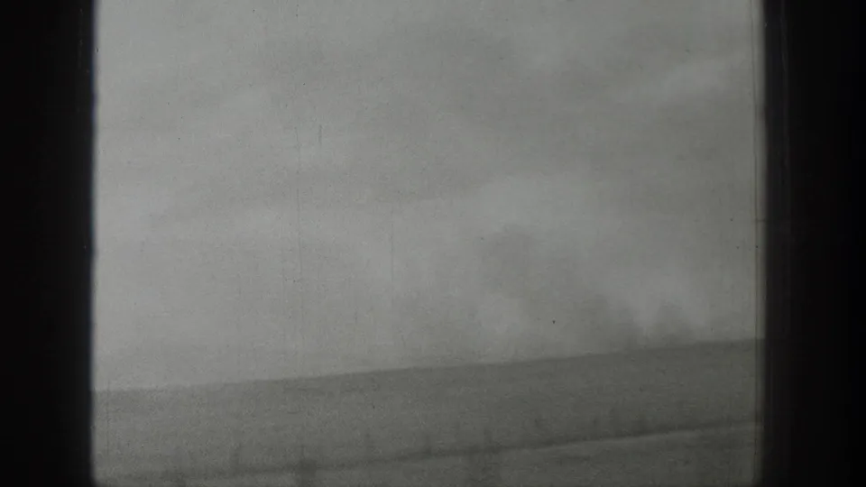 A grainy 8mm Wyoming storm view shows open land, low horizon, and drifting dust or haze through a window.