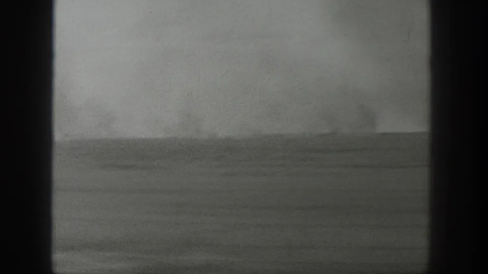 Archival 8mm view of a sparse Wyoming horizon with a faint vertical plume against a gray sky.