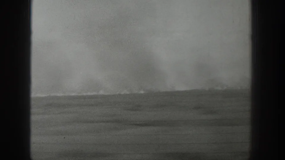 1939 Wyoming home-movie frame with a pale plume rising behind a low landscape, framed by dark 8mm borders.