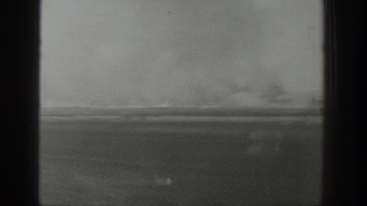 Hazy 1939 Wyoming home-movie view through dark window framing, with open ground and distant trees barely visible.