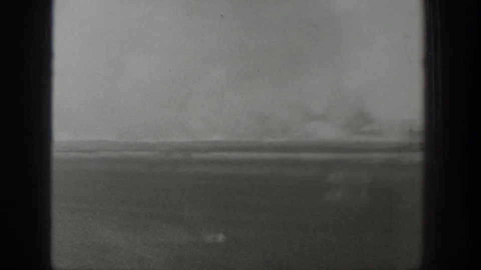 Hazy 1939 Wyoming home-movie view through dark window framing, with open ground and distant trees barely visible.