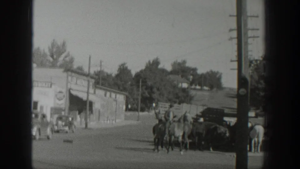 In 1939 Wyoming footage, a rider appears to lead several horses past storefronts, utility poles, pedestrians, and parked early automobiles.