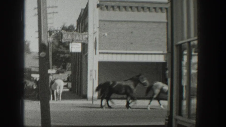 Near the end of the 1939 Wyoming clip, horses pass a storefront while a rider and utility pole frame the street-side view.
